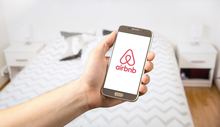 A person holding an airbnb phone with the airbnb logo on it.